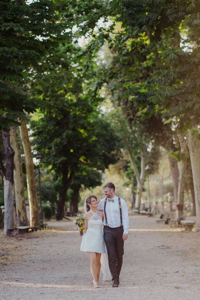 Couple walking down a path surrounded by tall trees in Villa Borghese.
