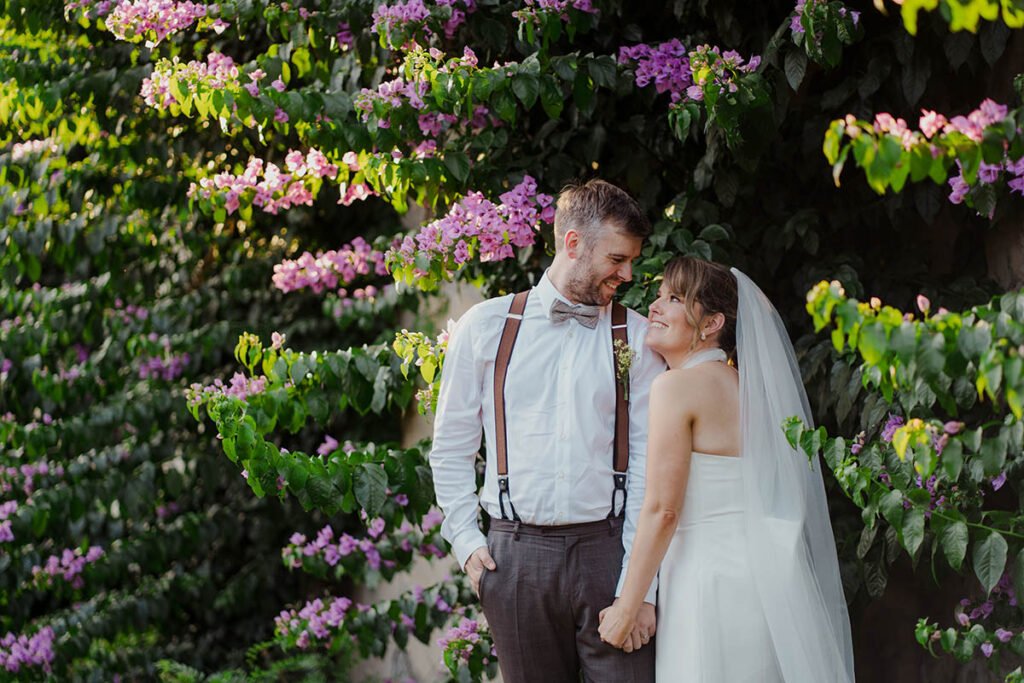 Couple smiling under a blooming wall of purple flowers.