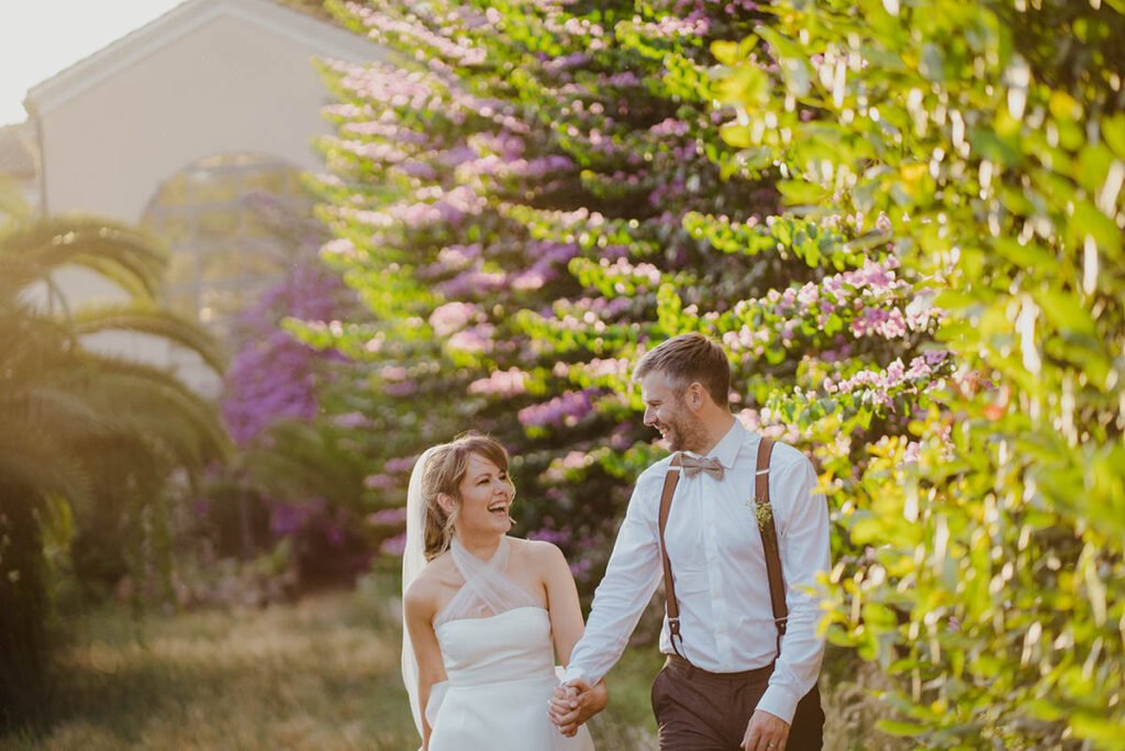 Bride and groom walking hand in hand in a garden with vibrant flowers.