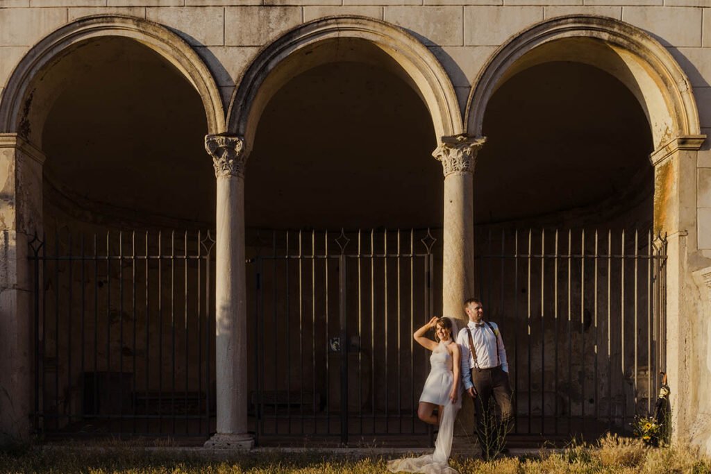 Bride and groom standing under historic arches in Rome.