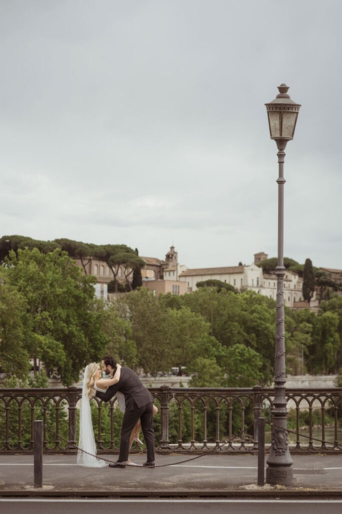 Couple kissing on a Roman bridge with city views – romantic Rome elopement captured by destination photographer