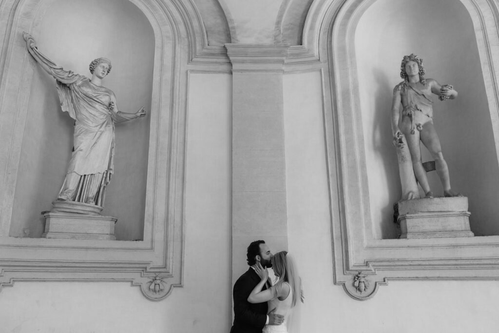 Bride and groom kissing under marble statues in a Roman palace – fine art photography by Rome elopement expert