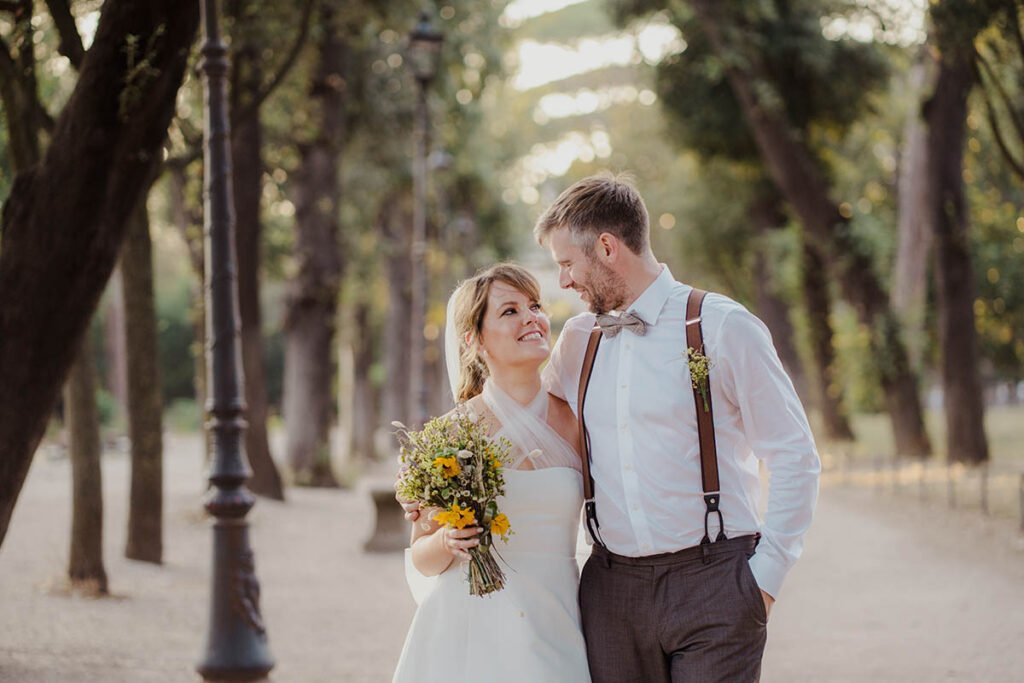 Bride smiling while holding bouquet and groom kisses her on the temple.