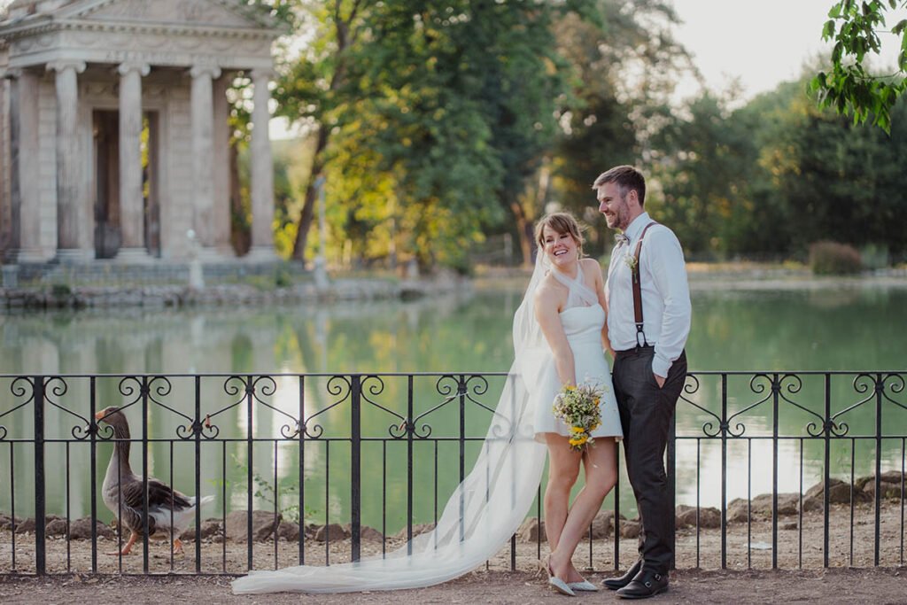 Couple holding hands near the lake and temple in Villa Borghese.