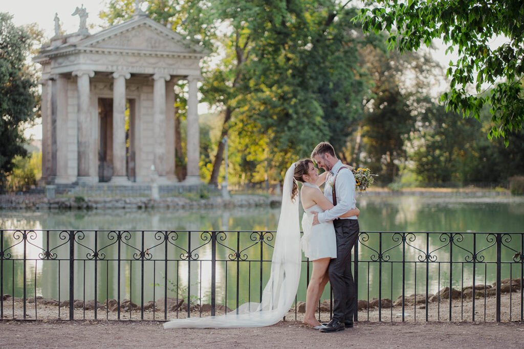 Couple standing near a lake and stone temple in Villa Borghese.