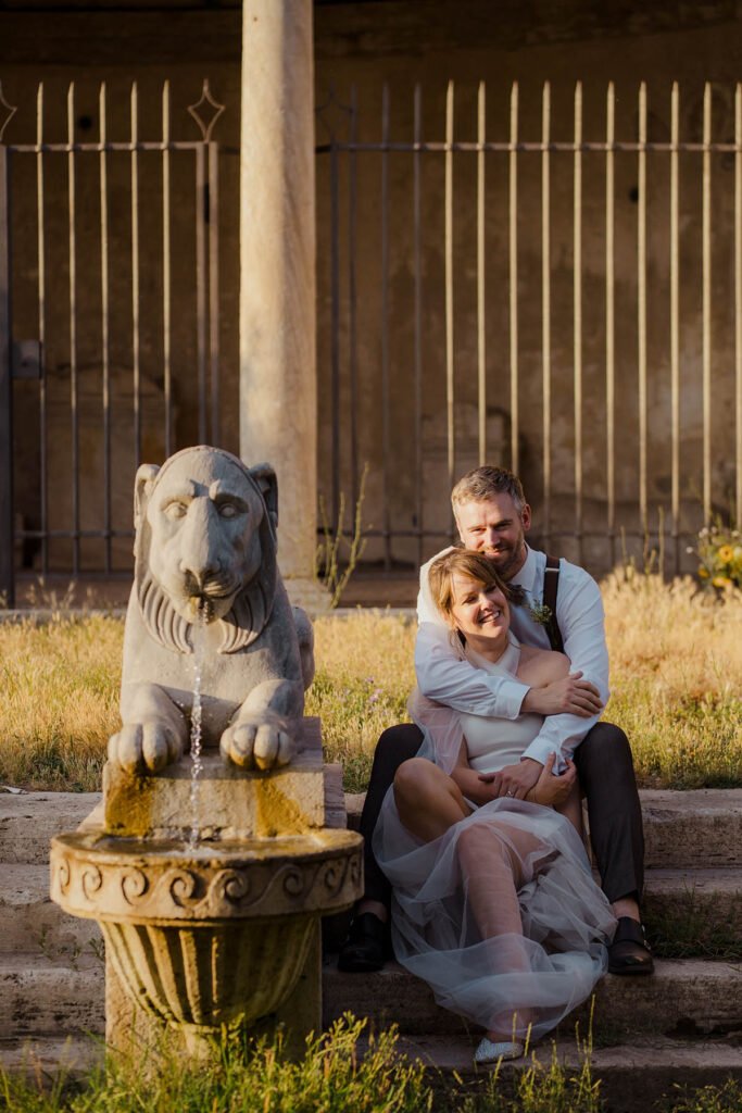 Bride and groom seated in front of a stone lion statue.