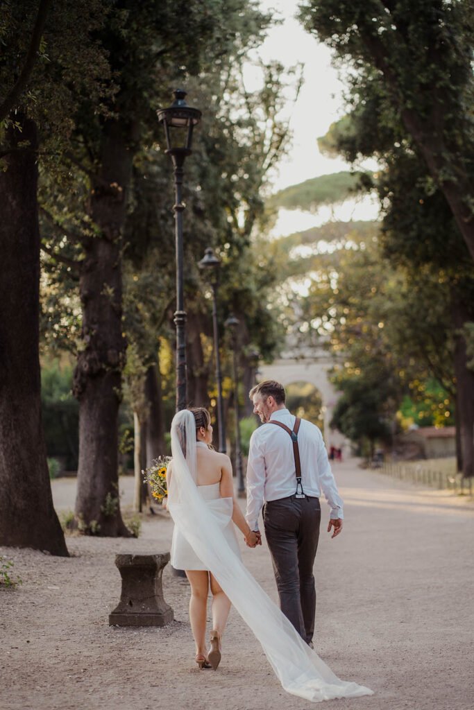 Couple walking through tall trees in Villa Borghese during their Rome elopement.