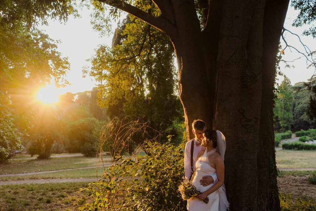 Bride and groom standing by a tree in golden light at sunset.
