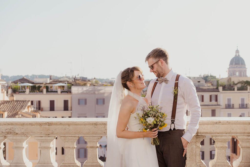 Bride and groom on a Roman rooftop with dome in the background.