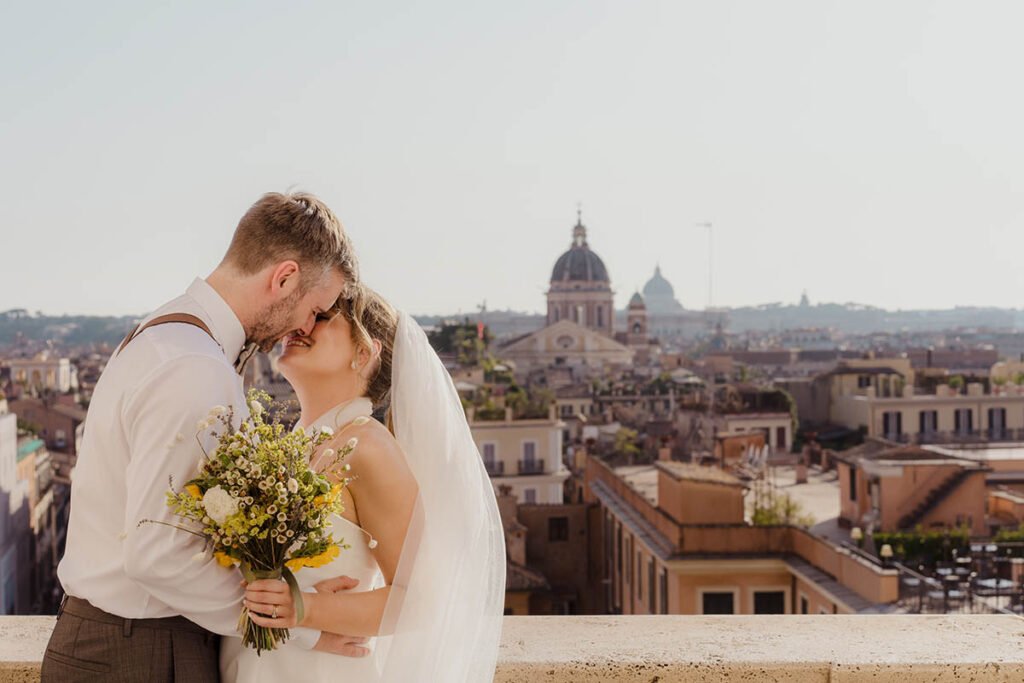 Bride laughing while groom kisses her cheek and holds bouquet.