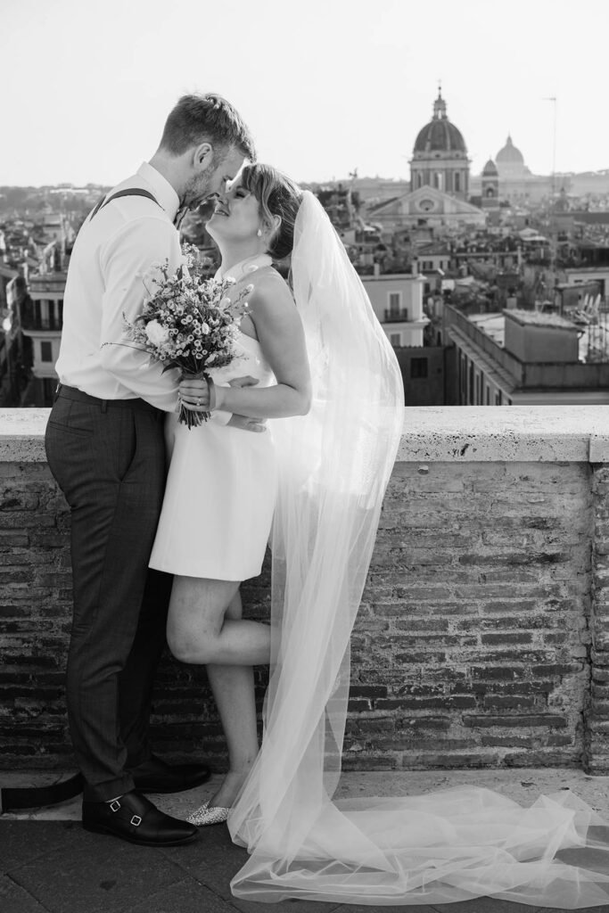 Couple kissing on a rooftop in Rome, with bride’s veil flowing.