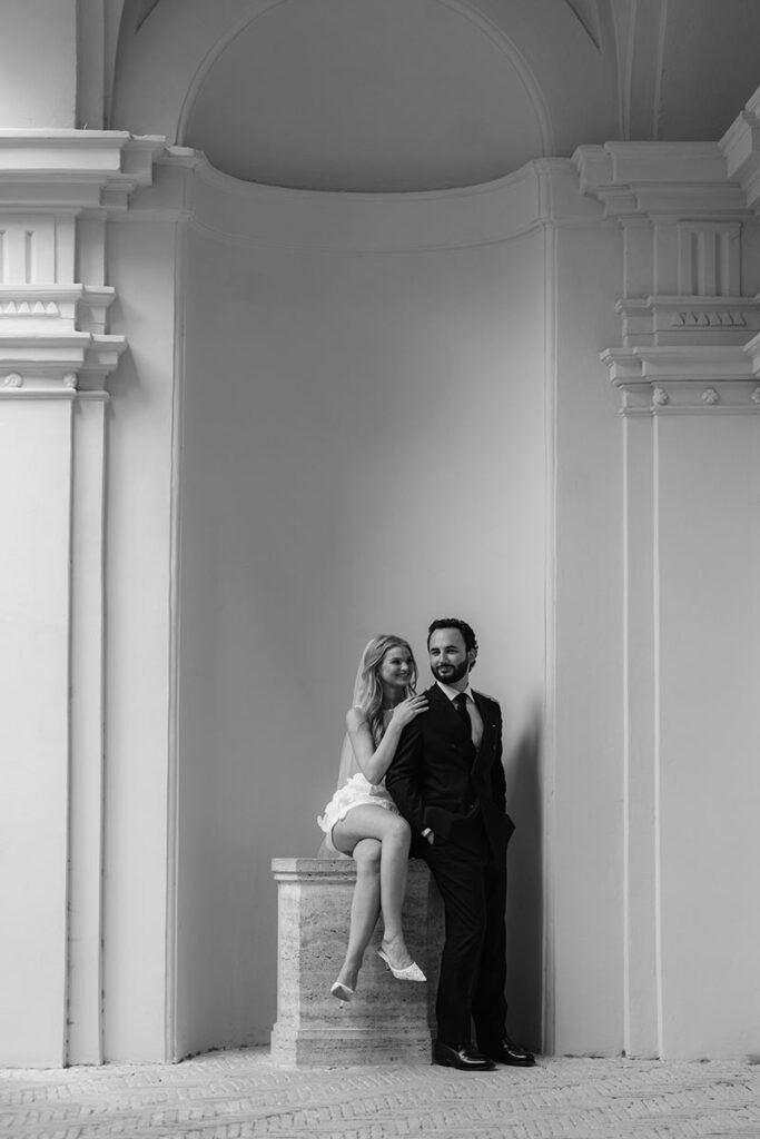 Bride sitting next to her groom in a Roman architectural alcove – elegant pose by elopement photographer in Rome