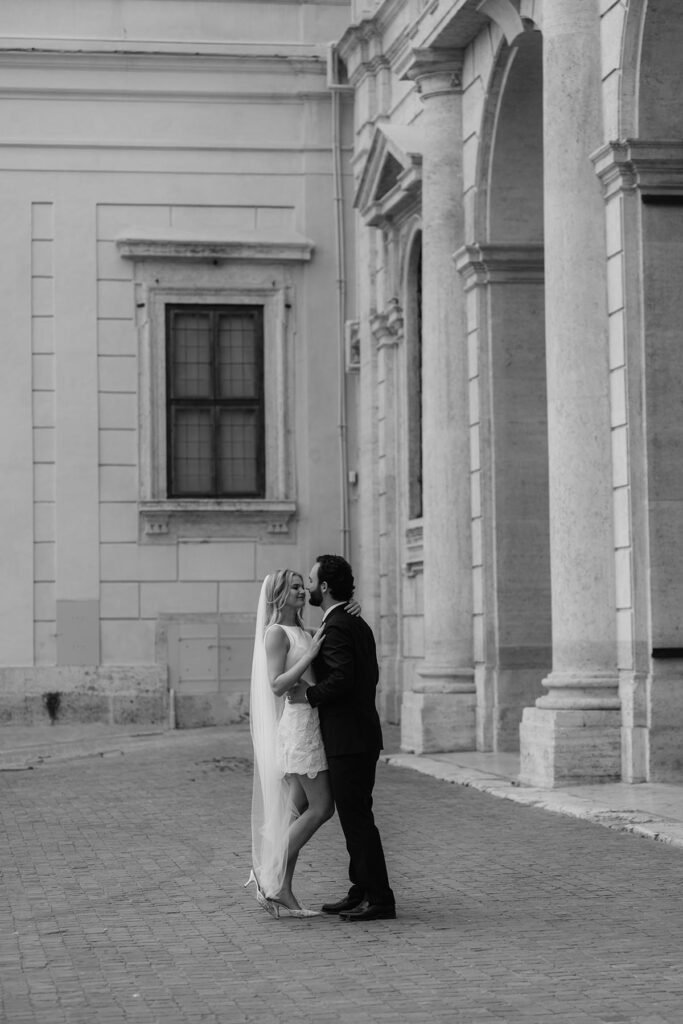 Groom kisses his bride on a cobblestone street near a Roman palace – authentic moment from an elopement in Rome