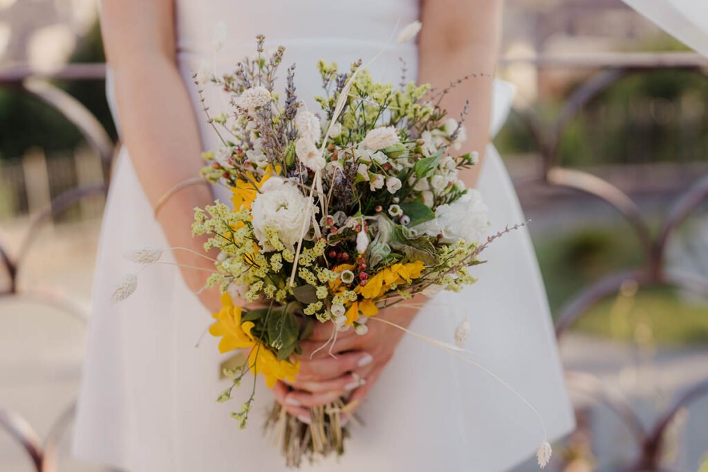 Close-up of bride holding a wildflower bouquet in a white mini dress.