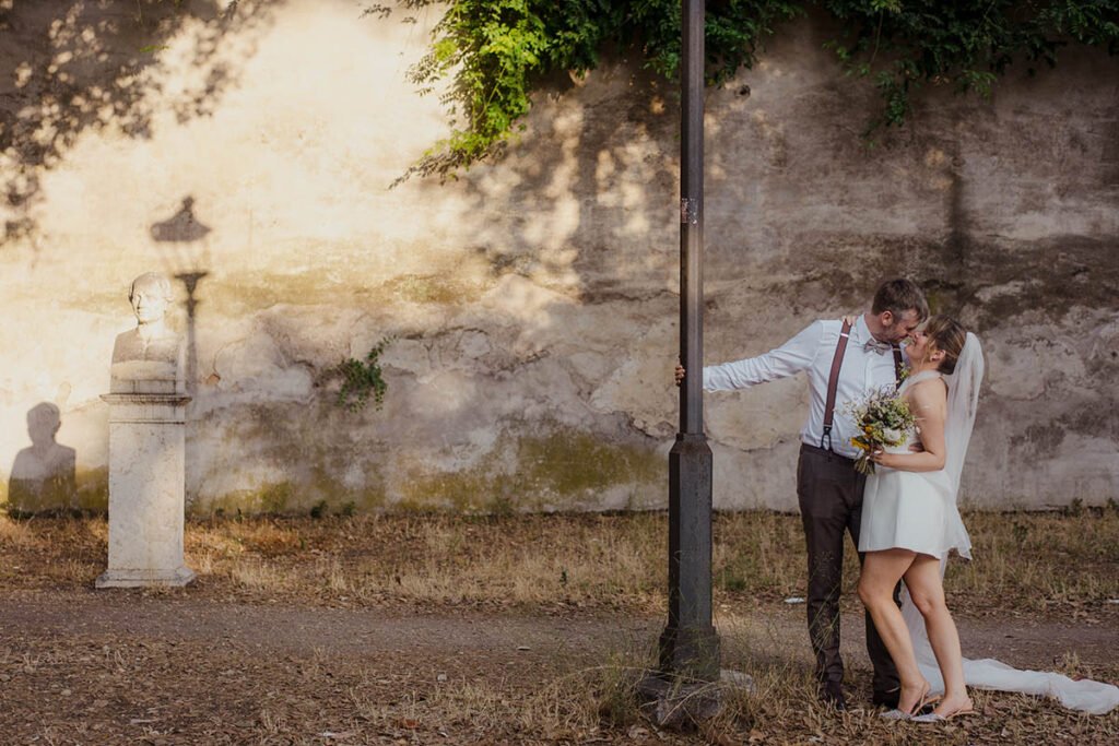 Bride and groom kissing under a vintage lamppost in Villa Borghese.