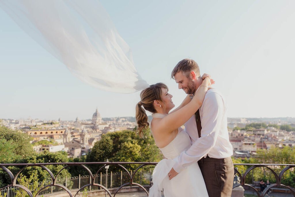 Groom holding the bride with her veil flying in the wind above Villa Borghese.