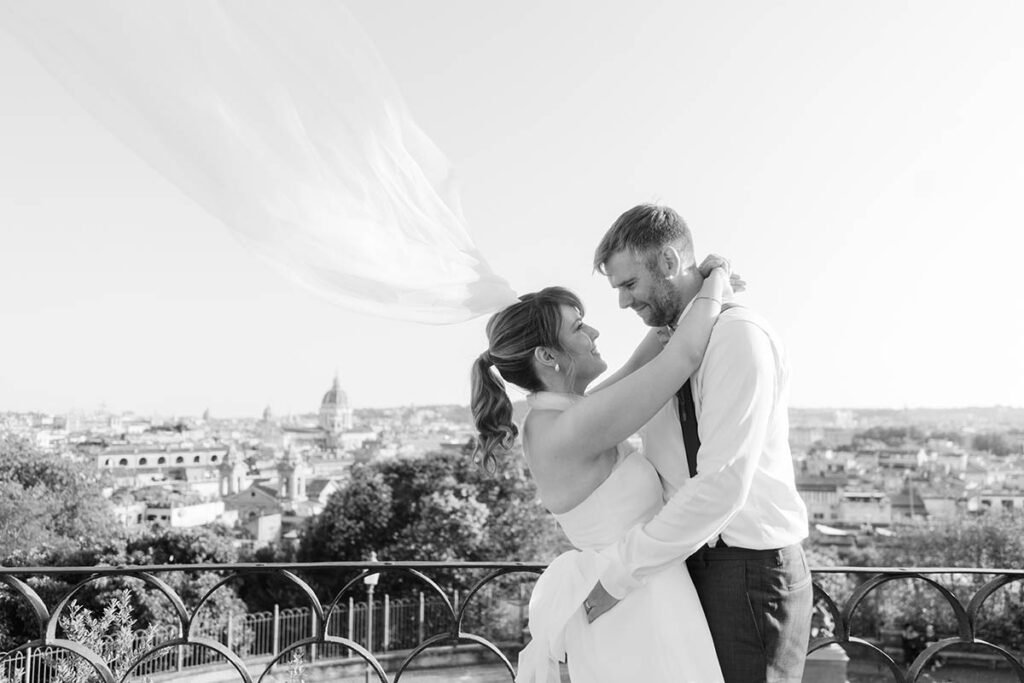 Black and white photo of couple smiling and embracing with Rome skyline behind.