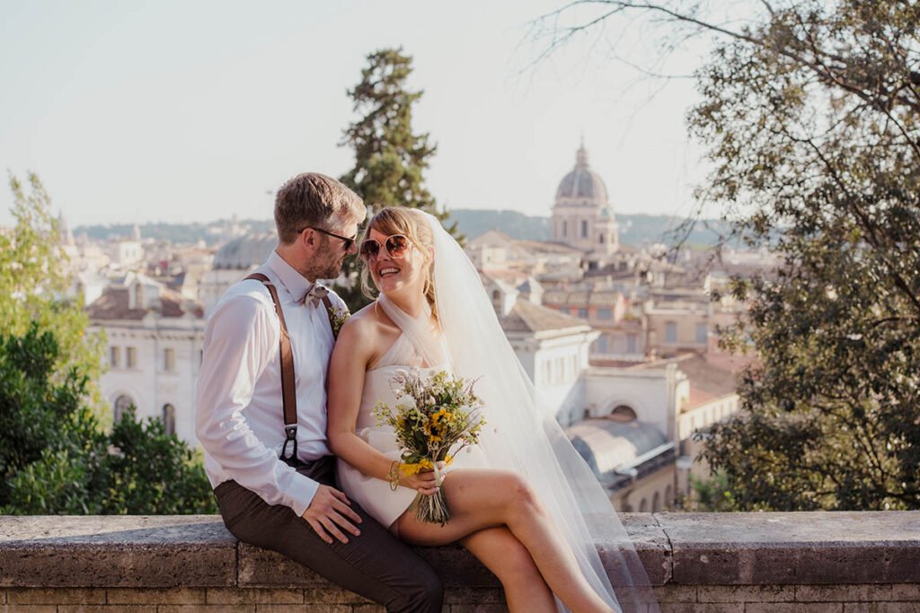 Couple sitting on a low wall overlooking the city with bouquet in hand.