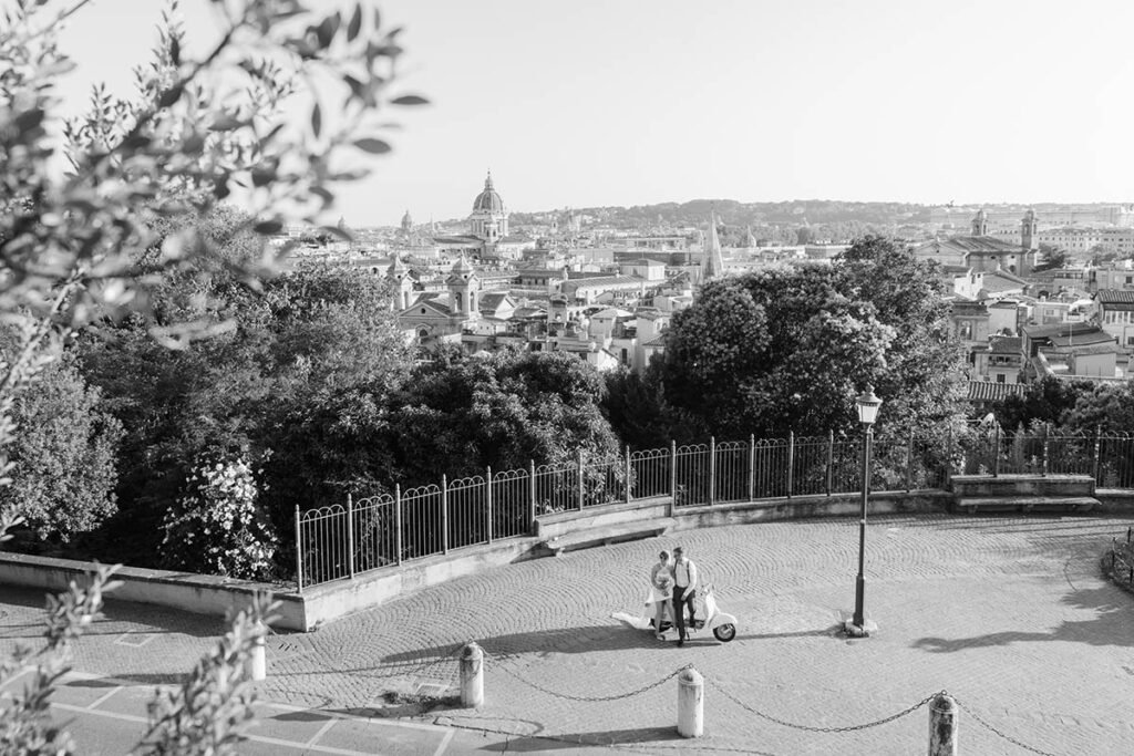 Black and white photo of a couple on a Vespa in front of Rome’s skyline.