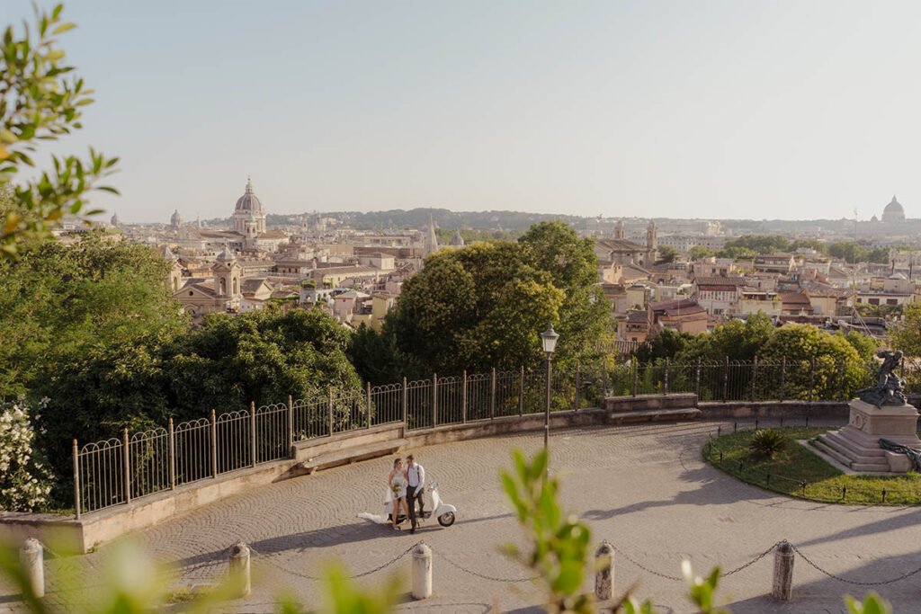 Couple riding a white Vespa through Rome with the skyline behind them.