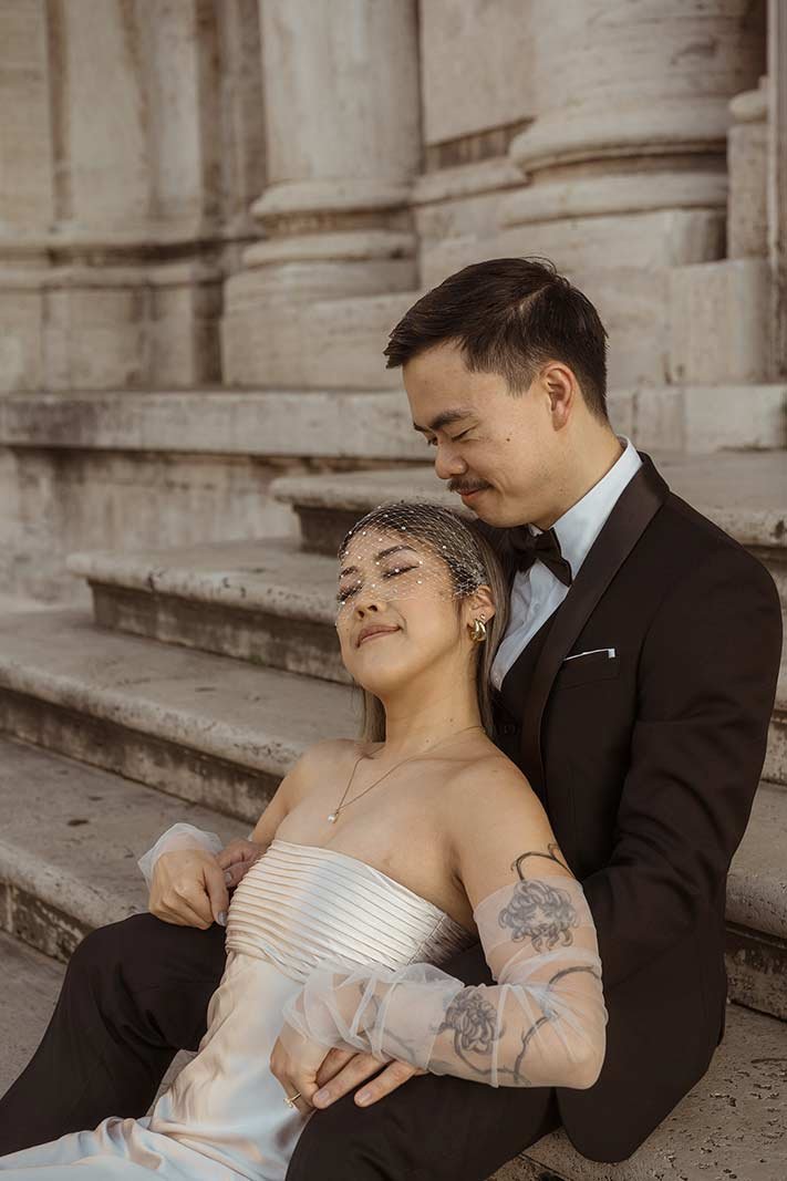 Bride leaning on groom’s chest on stone stairs during Rome elopement