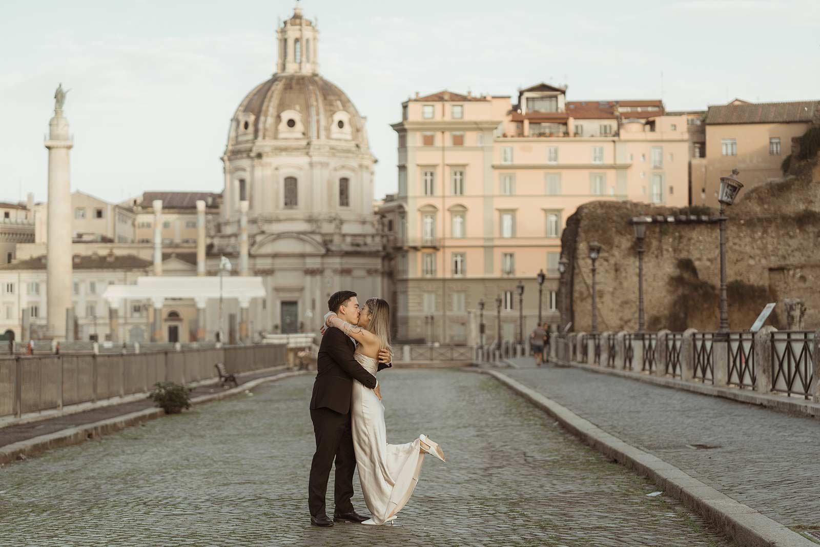 Couple kissing on cobblestone street with Trajan’s Column in the background during Rome elopement