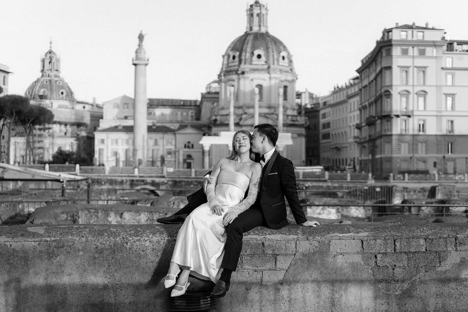 Rome elopement photo of bride and groom sitting on a wall at the Imperial Forum