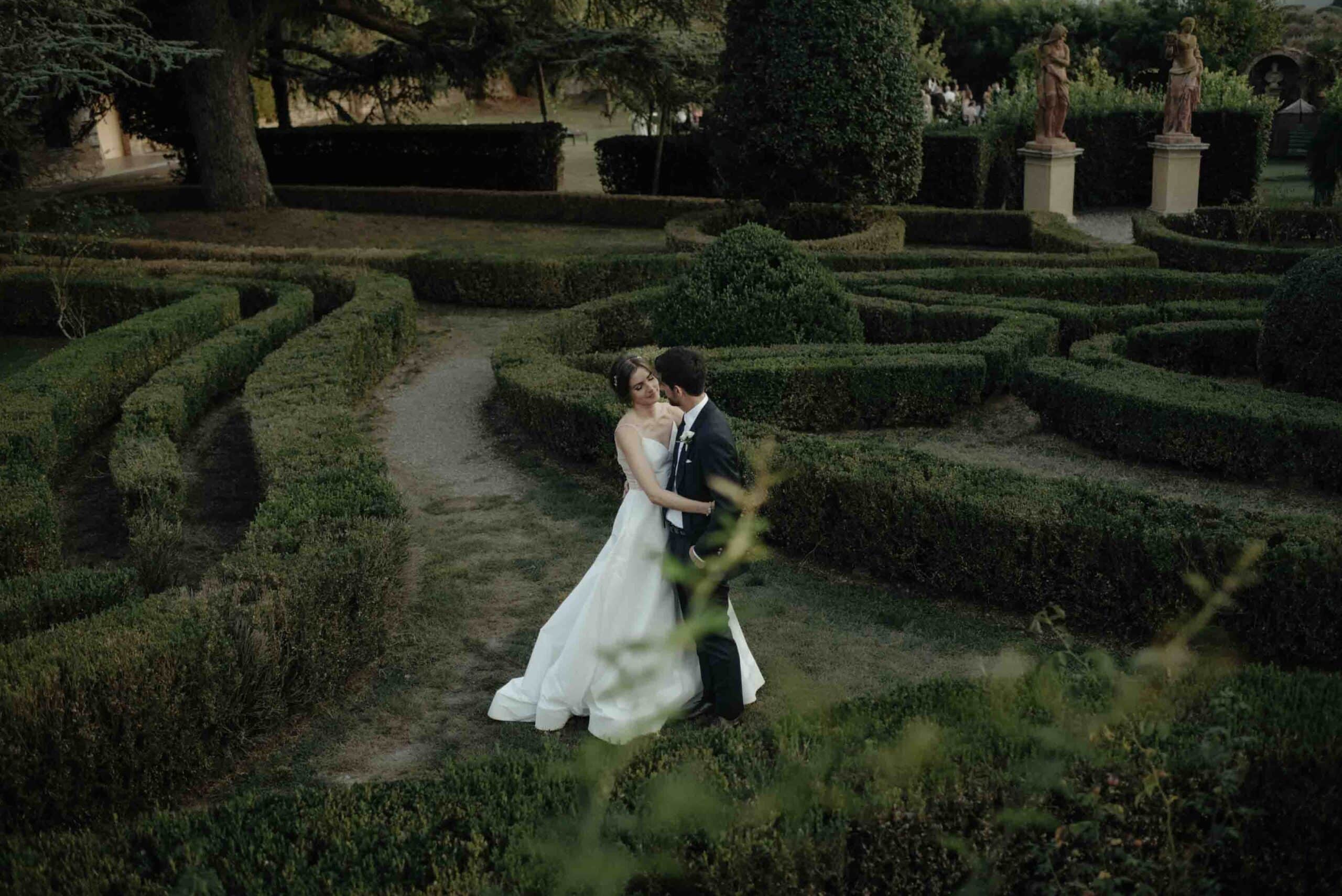 Bride and groom embracing in the Italian gardens of a luxury wedding villa in Tuscany.